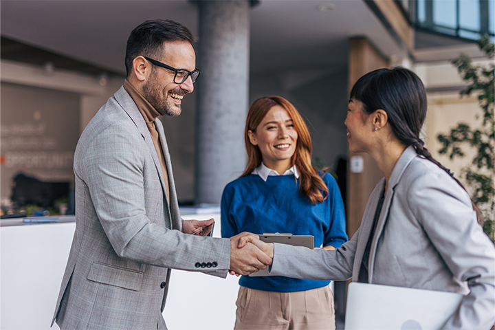 Female engineer holding a laptop meeting a man and woman and shaking the man's hand